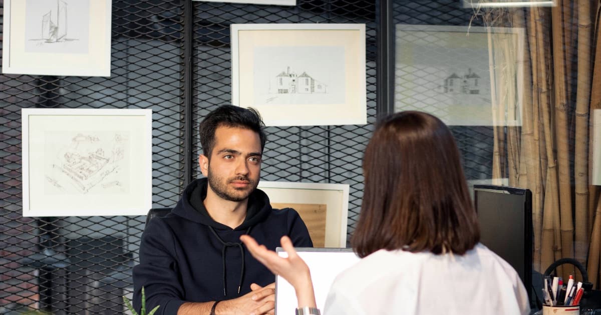 A candidate mid-answer at a desk while the recruiter interviewing him listens