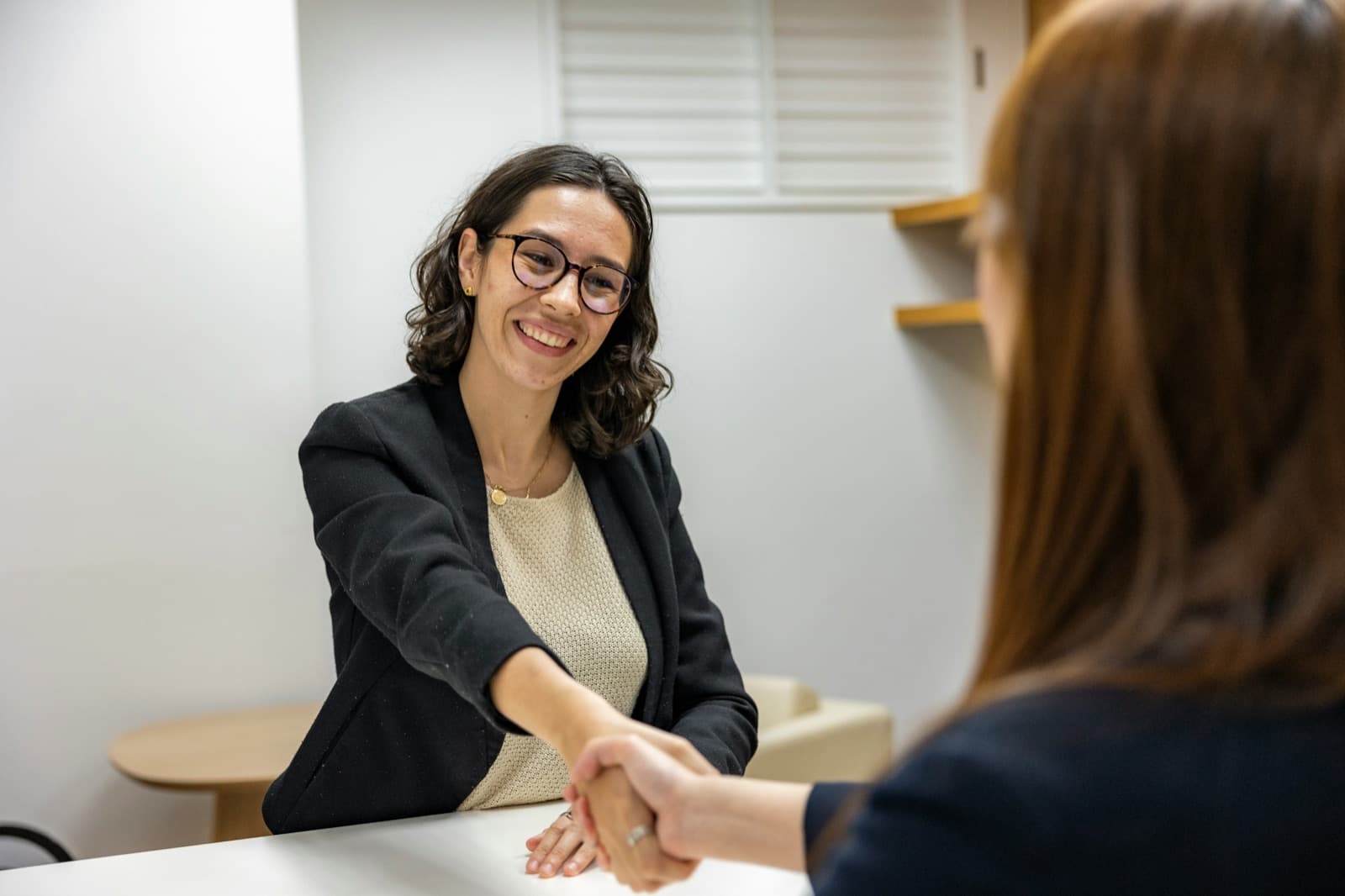 A hiring manager shaking hands with a candidate across a desk at the end of an interview